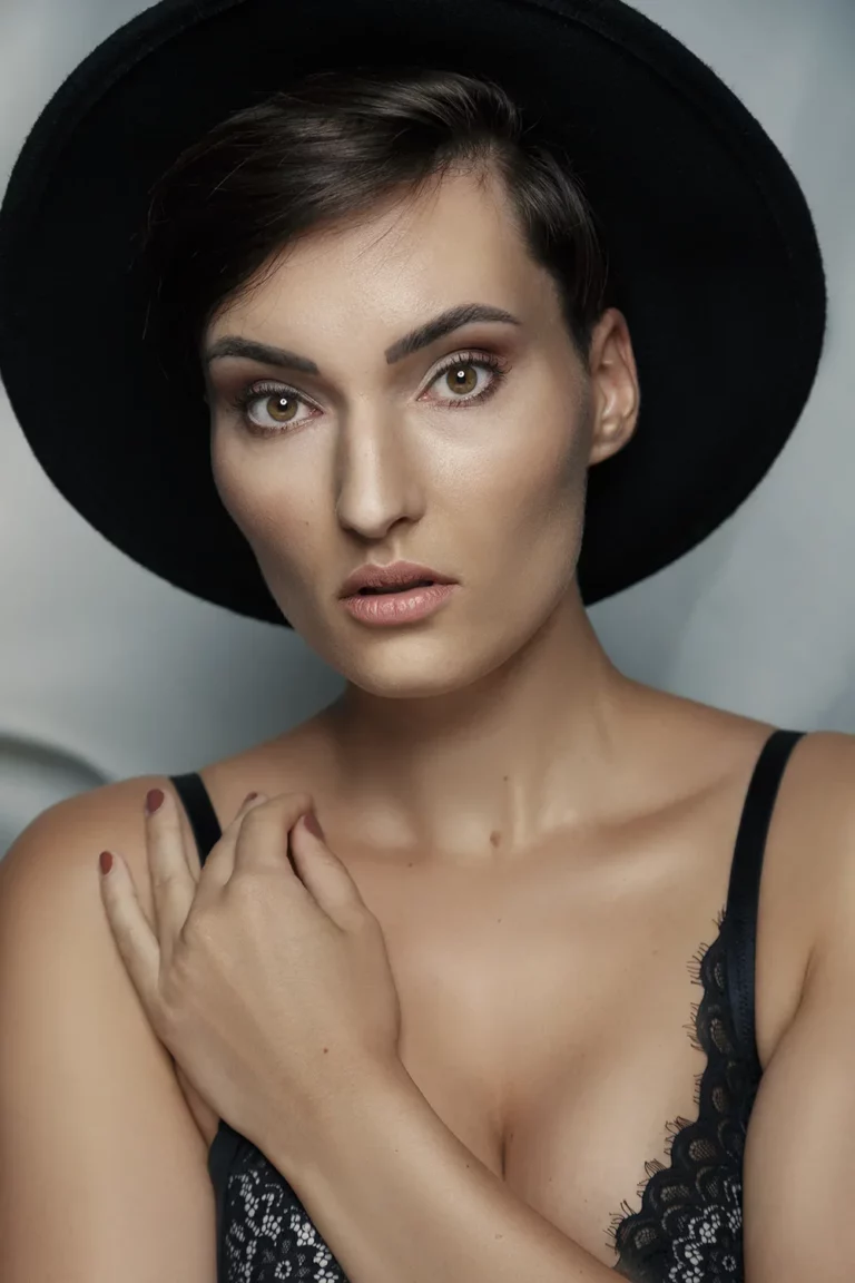 Model in schwarzem BH und Hut blickt ernsthaft in die Kamera vor einem dunklen Hintergrund.