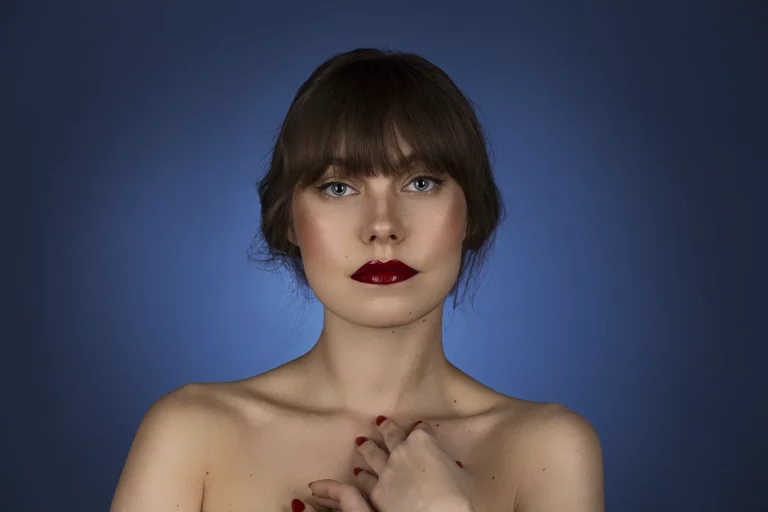 Porträt eines Models mit rotem Lippenstift und dunklem Haar vor einem blauen Hintergrund.